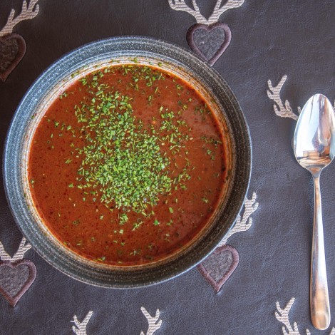 A bowl of red soup with herbs stands on a base decorated with deer antlers, with a spoon next to it.