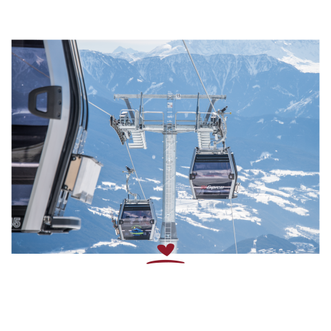 Two cable car cabins in front of snow-covered mountains and blue sky, one cabin partially in the foreground on the left.