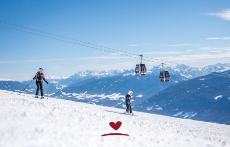 Children skiing on the slopes. In the background, two cable cars and a snow-covered mountain landscape under a blue sky.