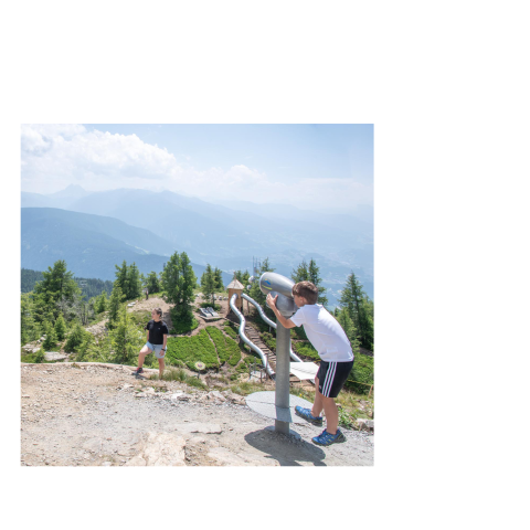 Two children on a mountain with a telescope and a slide, against a backdrop of wooded hills and mountains under a cloudy sky.