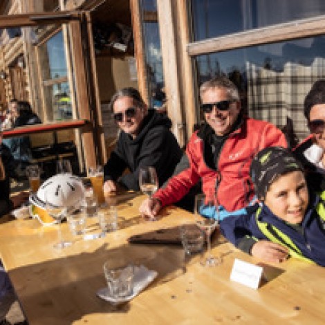 A happy family sitting at a table on the terrace in front of the mountain restaurant.
