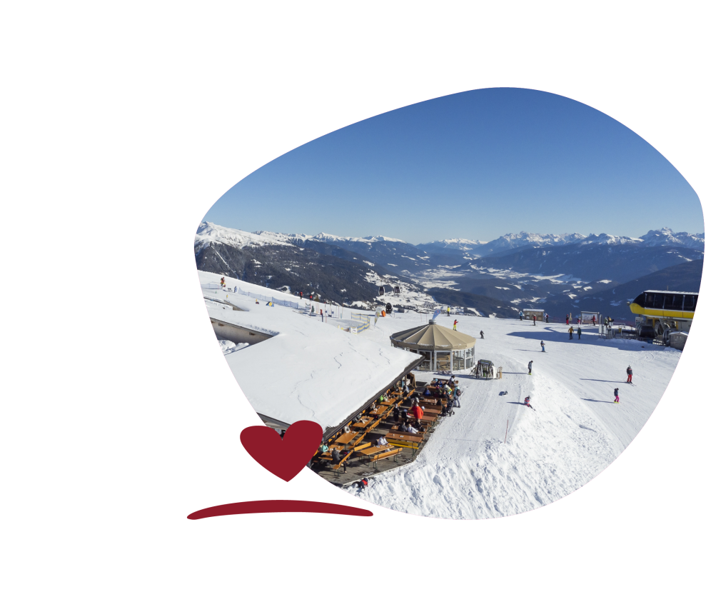 Mountain restaurant with sun terrace and several guests on snow-covered summit, mountain panorama and blue sky in the background.
