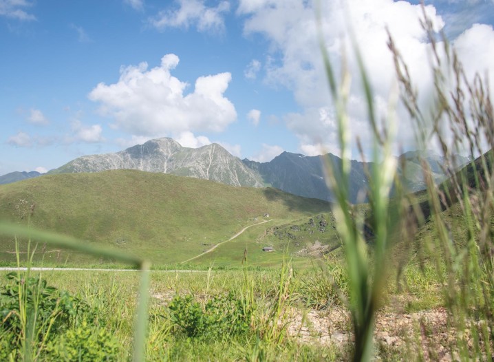 Mountains surrounded by green meadows under a blue sky with a few clouds.
