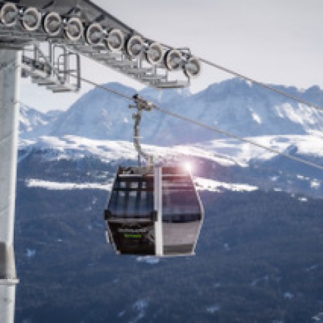 A gondola on a cable car and, in the background, a snow-covered mountain backdrop under a blue sky in the blur.