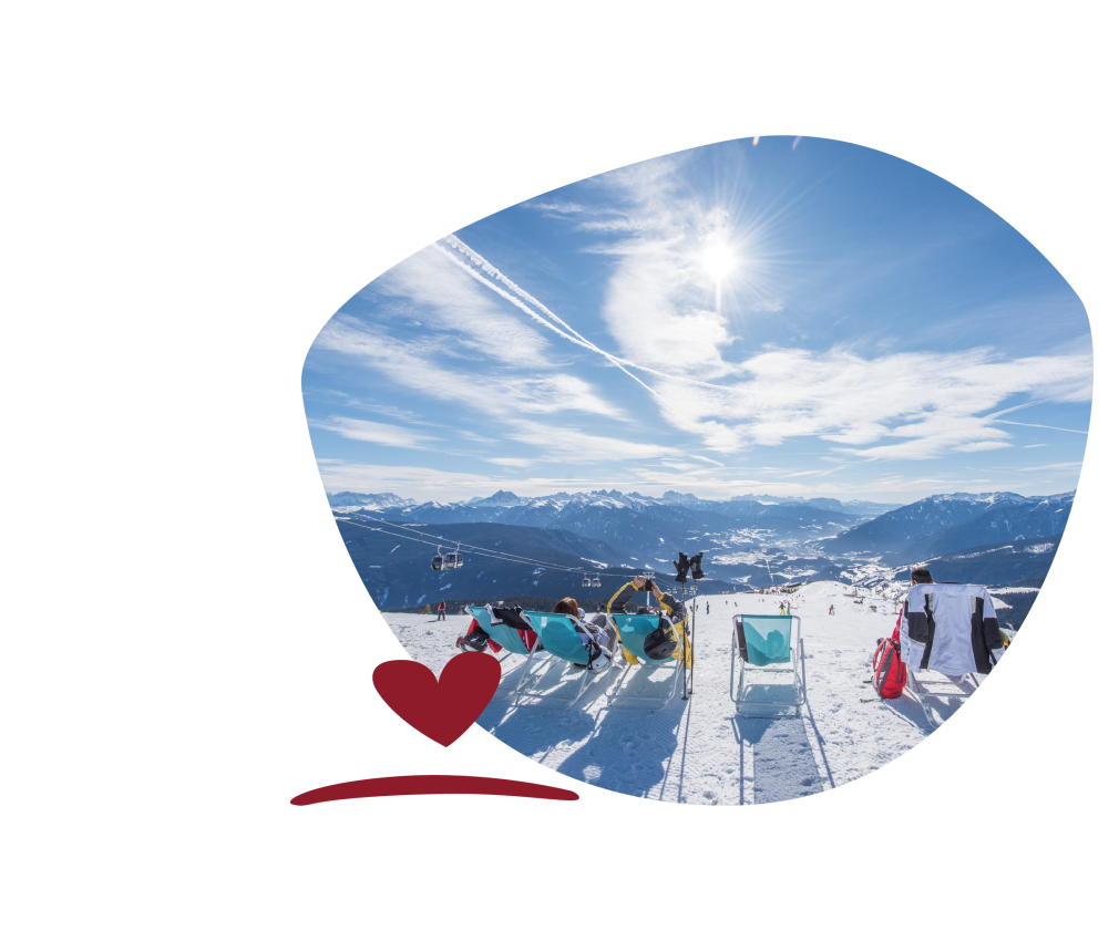 People sitting on deckchairs in the snow admiring the snow-covered mountains and valley beneath a blue sky with a few clouds.