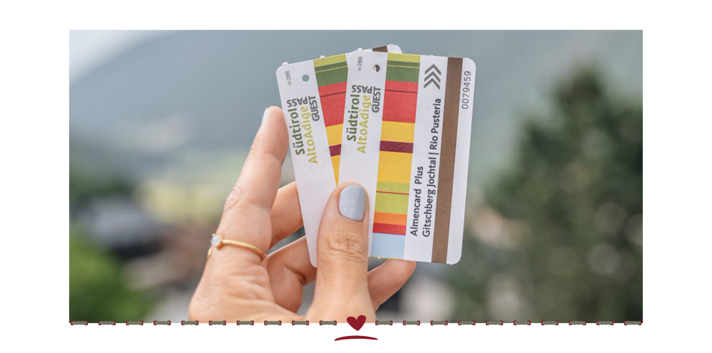 In one hand, two coloured tickets with the words ‘Südtirol, Alto Adige Pass. Almencard Plus.’
