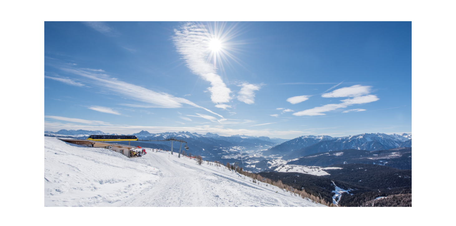 Snow-covered path leading to a cable car in a snowy landscape. Surrounded by mountain scenery under a blue sky and bright sunshine.