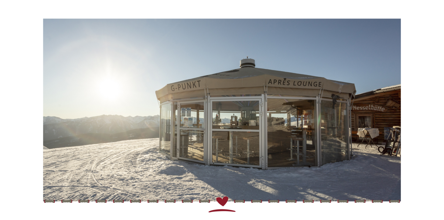 An après-ski lounge, a round building with a glass front, on a snow-covered mountain in the sunshine.
